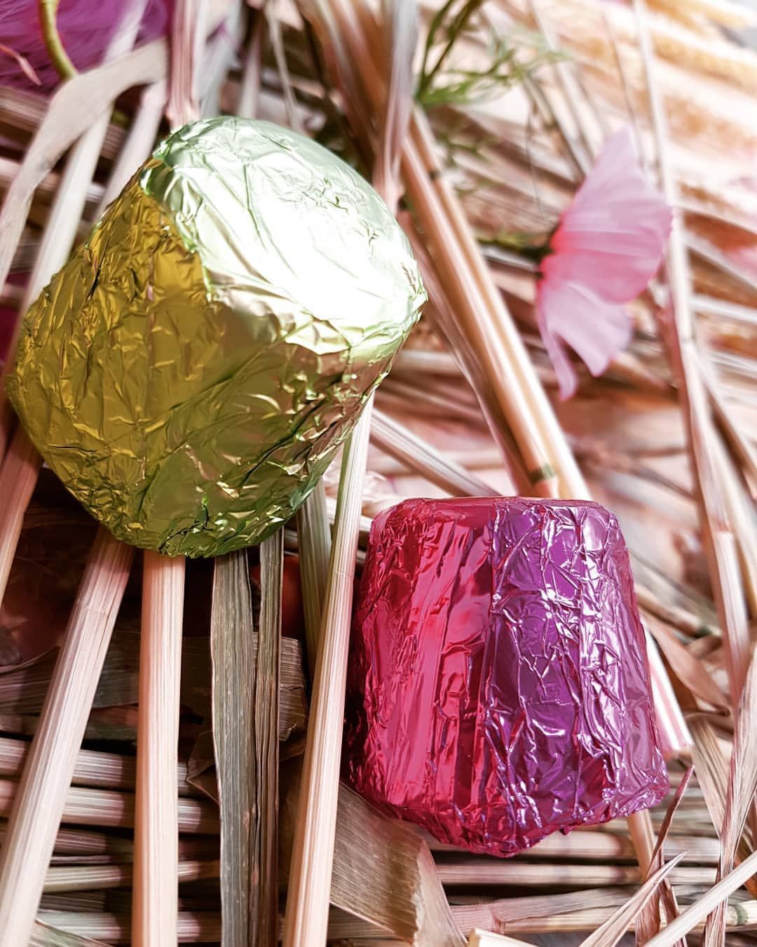 Deux bonbons emballés dans du papier d'aluminium, l'un vert et l'autre rose, reposent sur des roseaux secs.