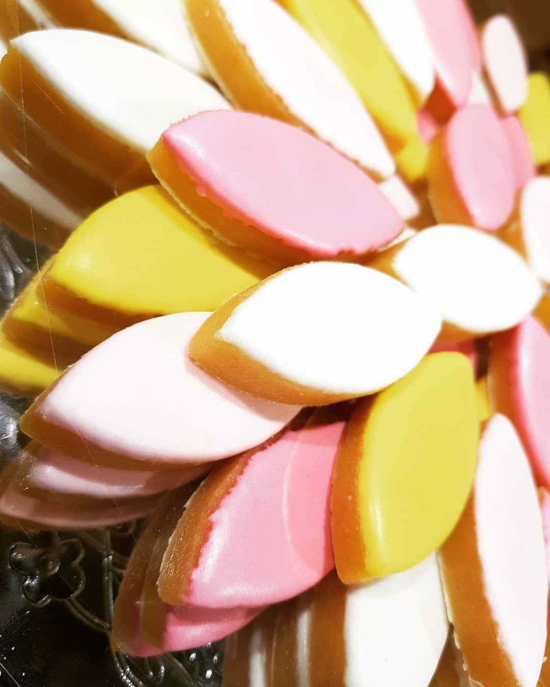 Calissons colorés disposés en forme de fleur sur une surface réfléchissante.