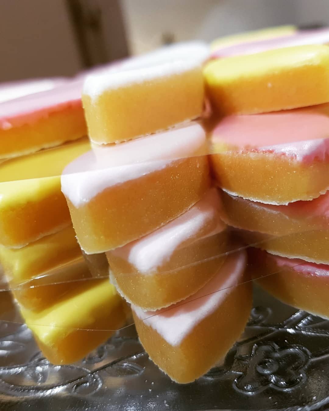 Gros plan sur des calissons colorés avec un glaçage blanc, rose ou jaune, empilés sur une surface réfléchissante.