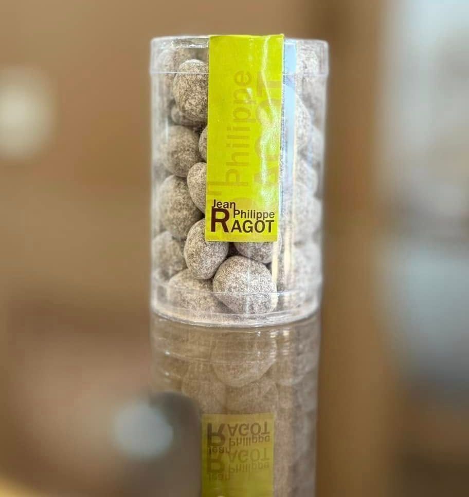 Un tube transparent de dragées avec une étiquette jaune sur une surface réfléchissante.