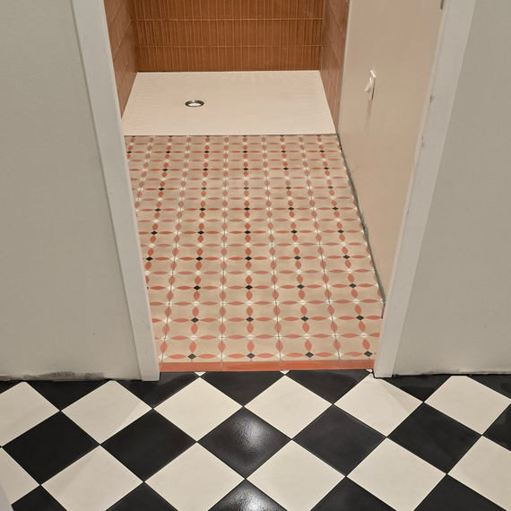 Couloir avec sol à damier noir et blanc menant à une cabine de douche carrelée avec bonde