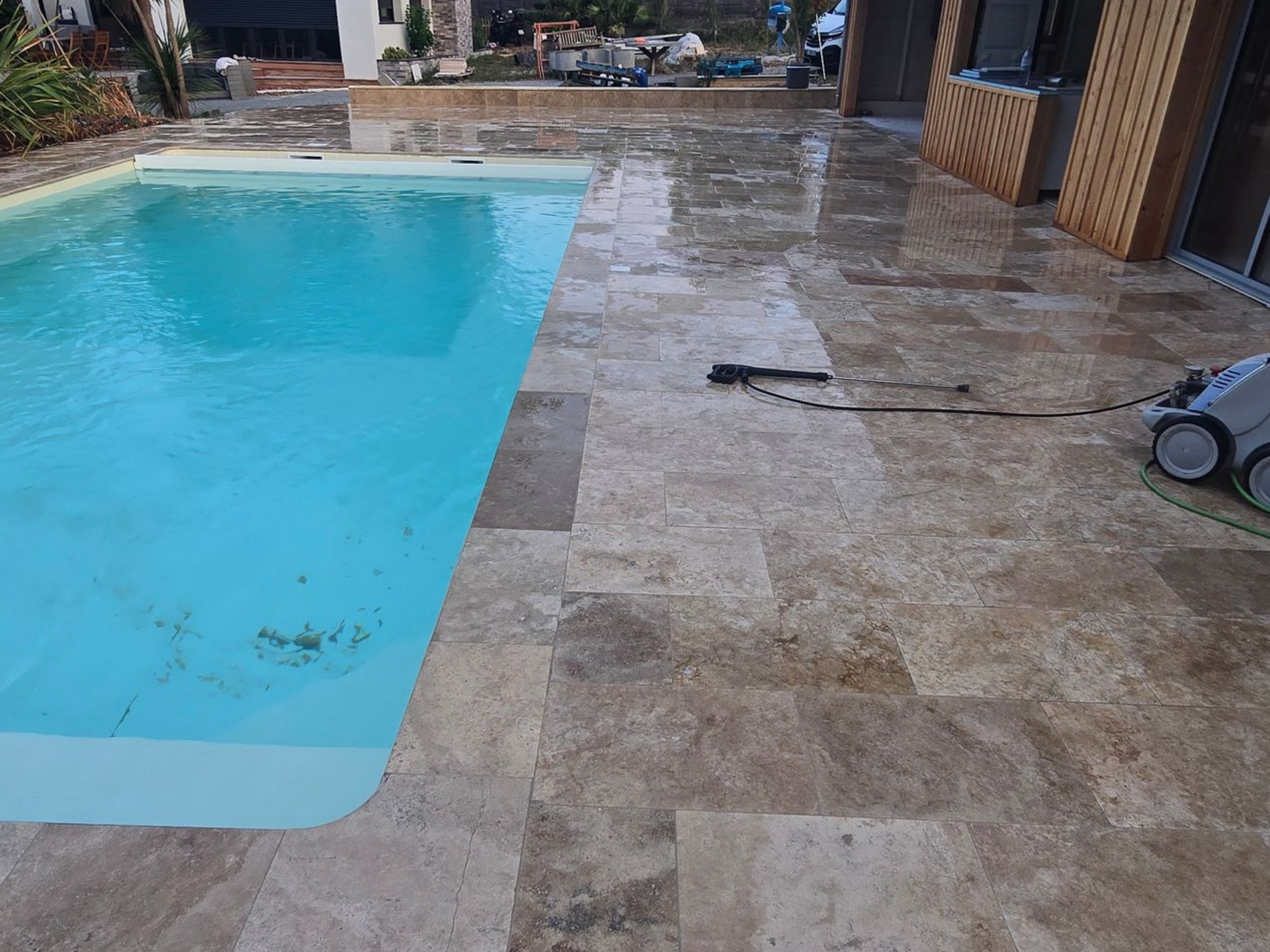 Piscine bleue à côté d'une terrasse en pierre avec un outil de nettoyage de piscine sur la droite.