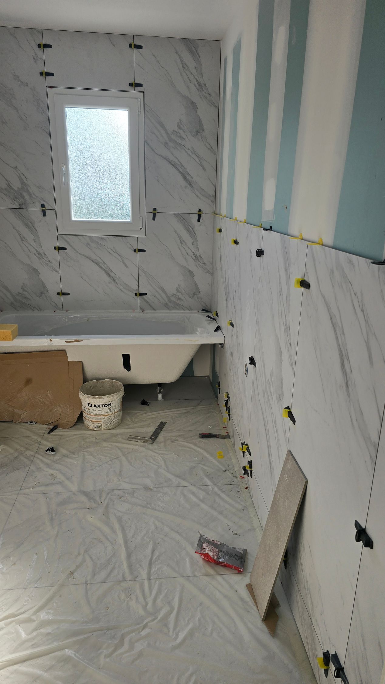 Salle de bains en rénovation avec carrelage blanc imitation marbre, baignoire et matériaux de construction au sol.