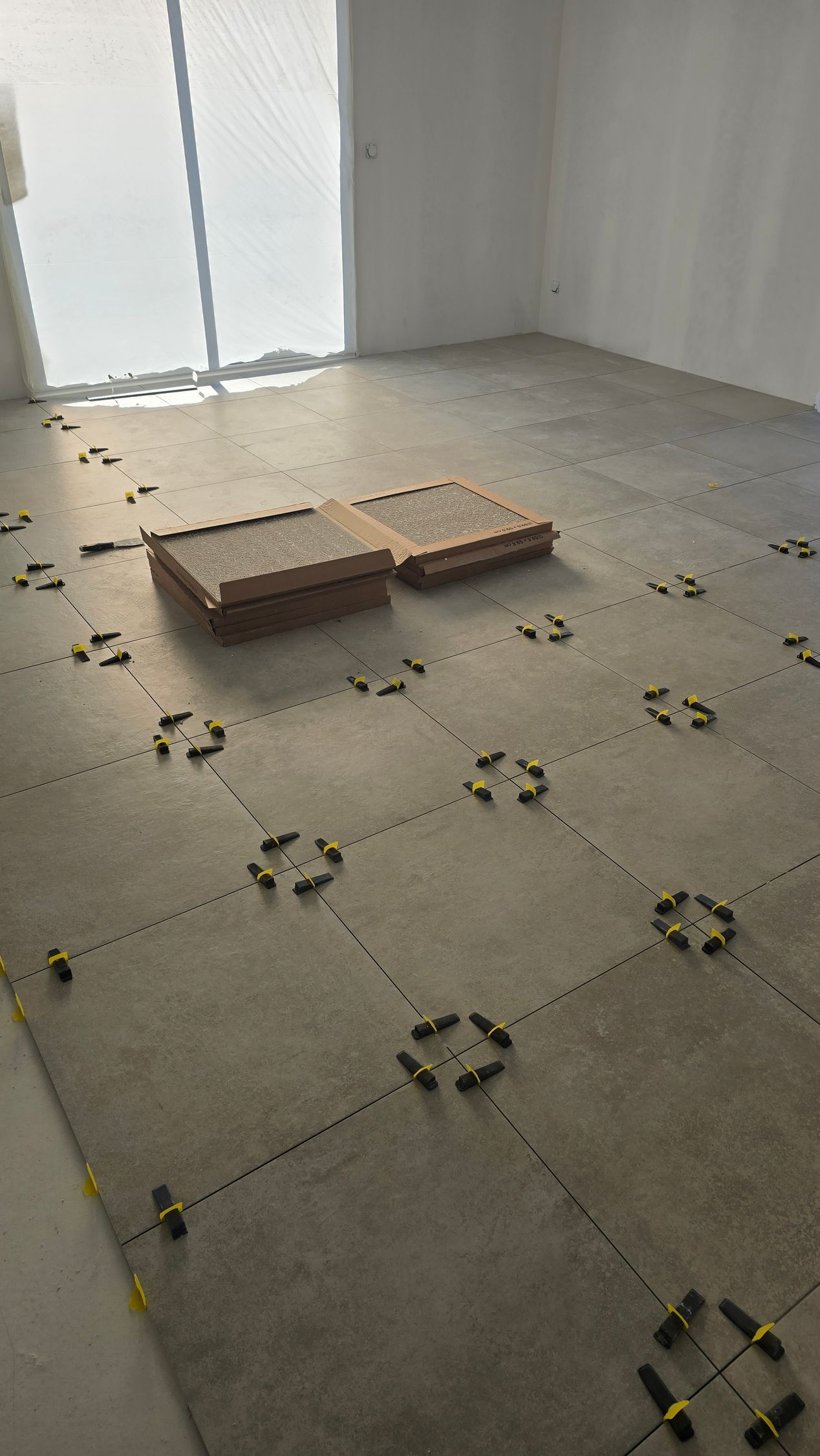 Pièce vide au sol non fini, avec des marqueurs entre les carreaux de carrelage et deux cartons empilés.