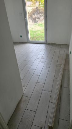 Pièce vide avec un sol carrelé inachevé et une porte ouverte donnant sur un espace extérieur.