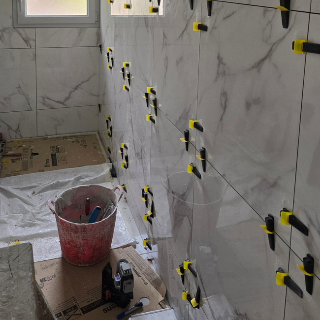 Salle de bains en rénovation avec carrelage mural imitation marbre, croisillons et outils au sol.