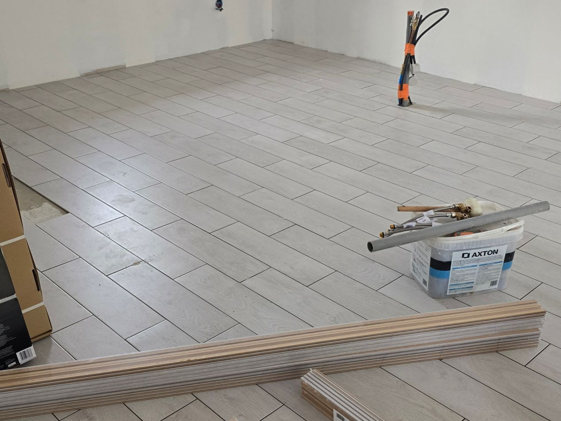 Sol carrelé en cours de pose avec outils, croisillons et carreaux empilés dans une pièce vide.