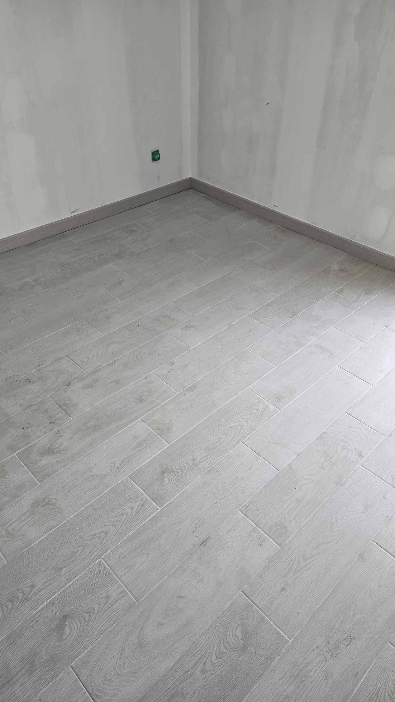 Pièce vide aux murs et au sol gris clair, laissant apparaître un coin et une plinthe.