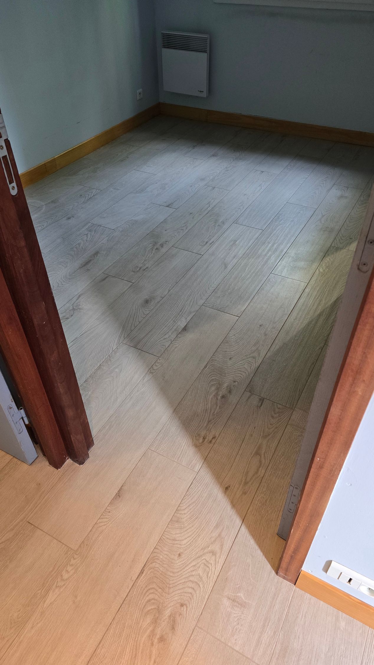 Pièce vide avec un parquet, des murs clairs et un radiateur mural.