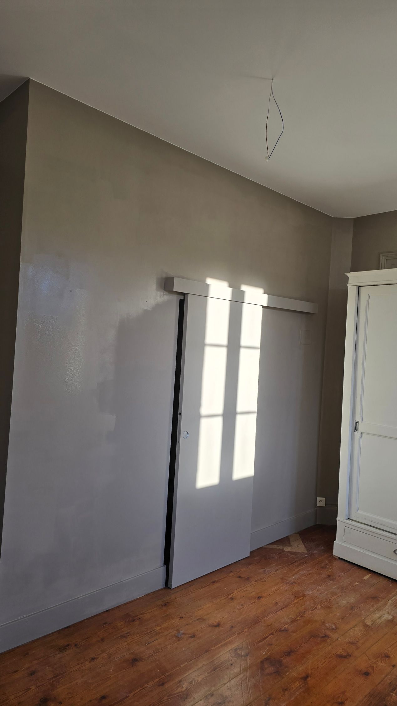 Pièce vide aux murs gris, au sol en bois.