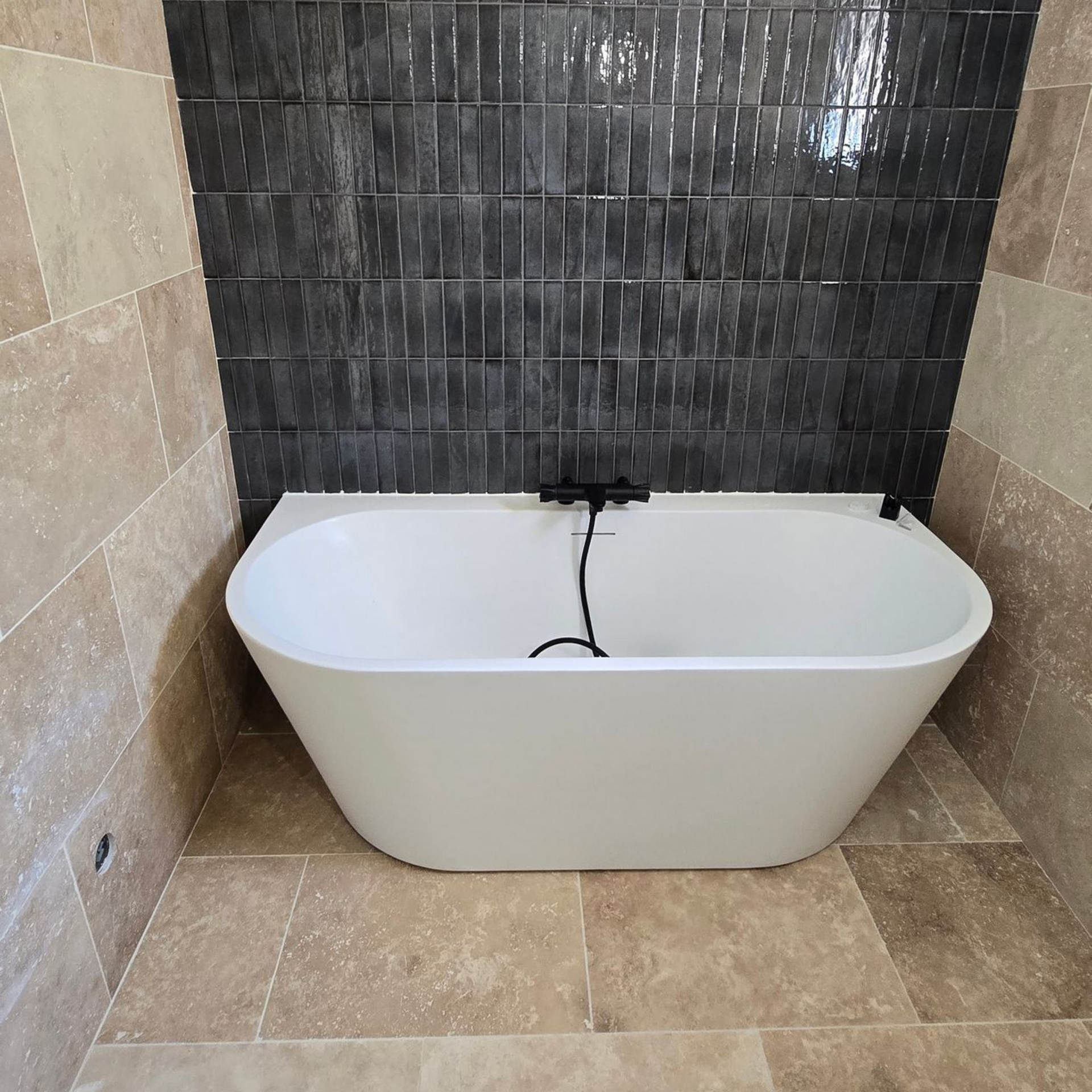 Baignoire blanche contre un mur d'accent carrelé foncé dans une salle de bains carrelée beige.