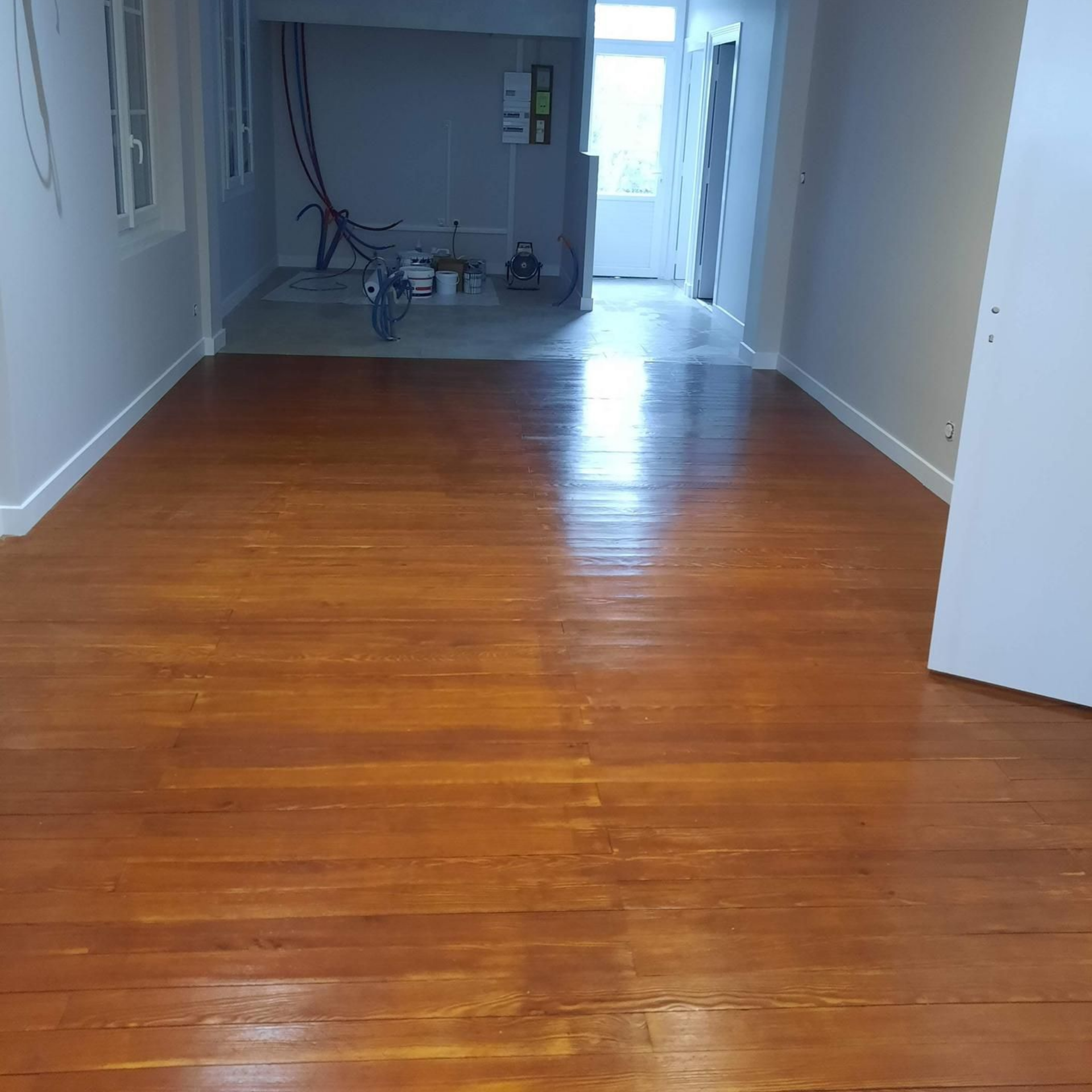 Pièce vide avec un parquet brillant et un couloir lumineux à l'arrière