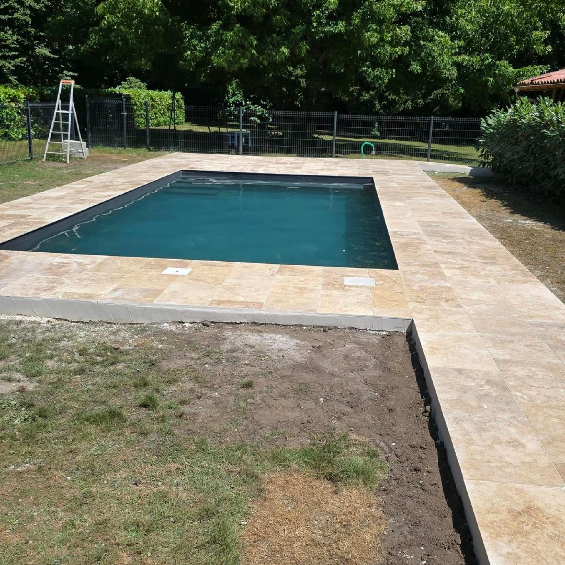 Piscine dans le jardin avec terrasse en pierre beige, pelouse et arbres en arrière-plan