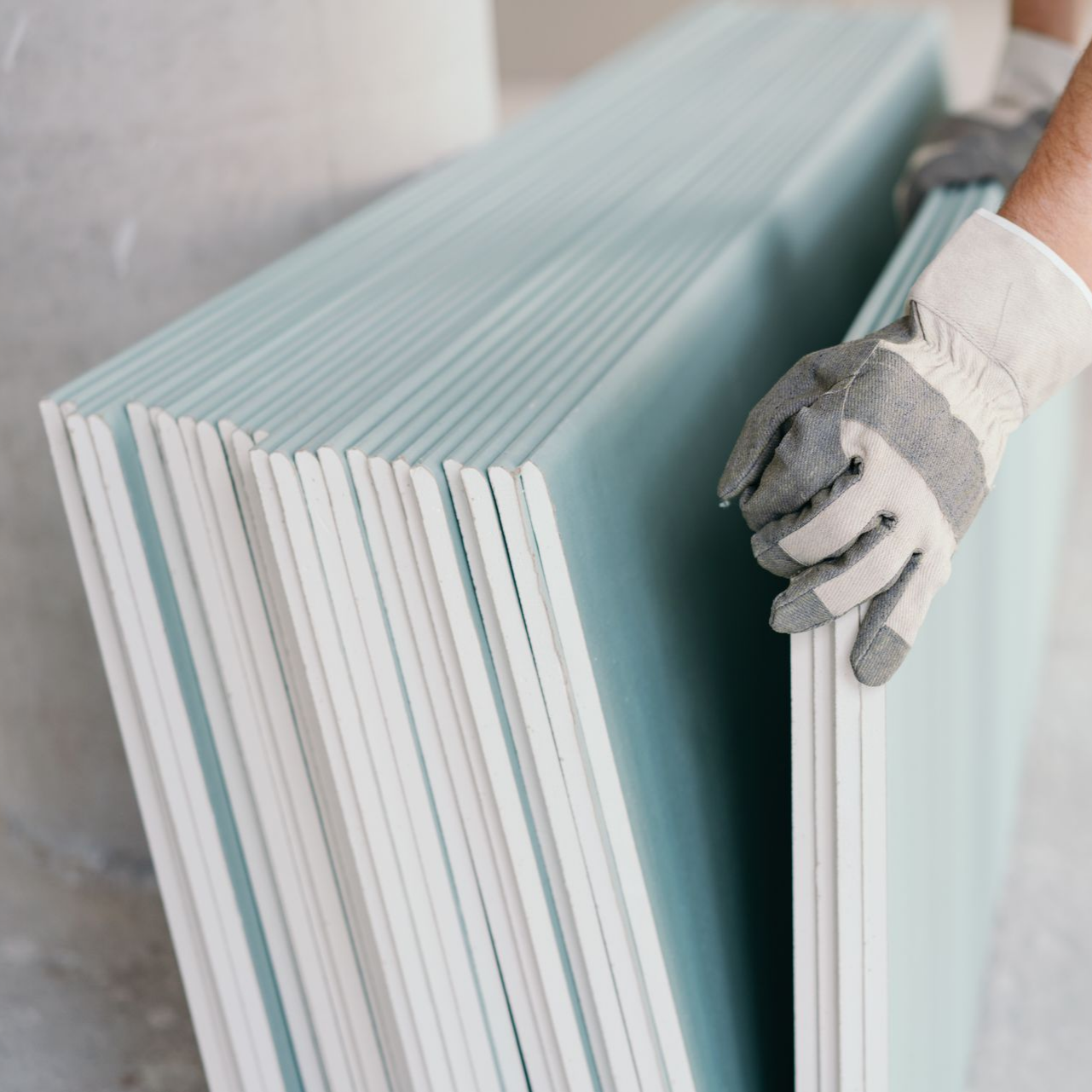 Main gantée tenant une pile de panneaux de plaques de plâtre.