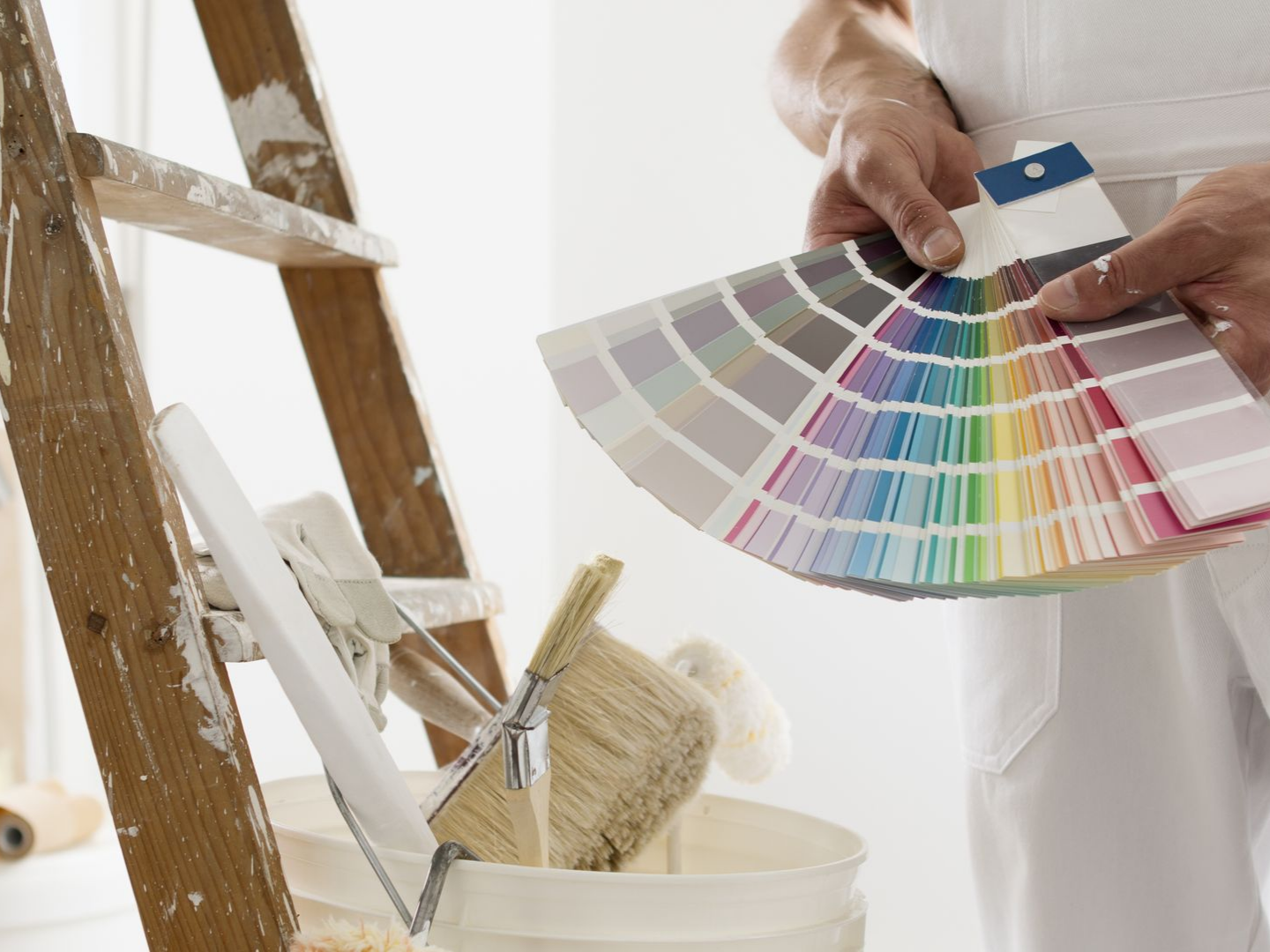 Une personne tenant un éventail d'échantillons de peinture à côté d'un chevalet et de pinceaux.