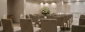 Elegante sala de conferencias con sillas beige dispuestas alrededor de las mesas y un centro de mesa floral blanco.