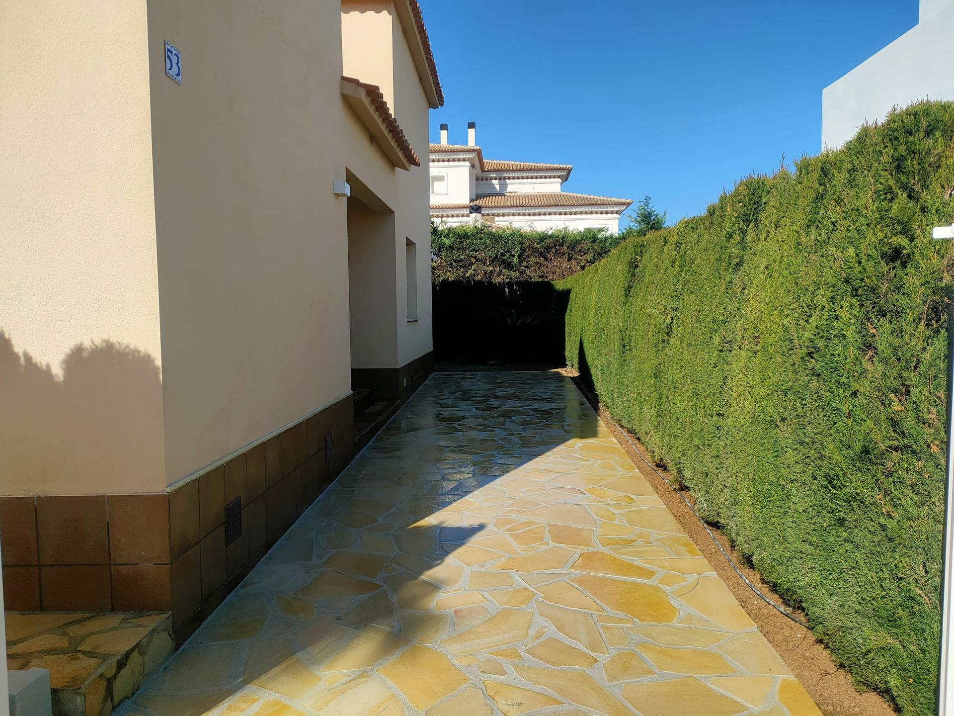 Un camino de piedra que conduce a una casa con un seto a lo largo del costado.