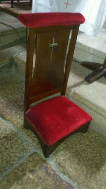 Una silla de madera para arrodillarse con un cojín rojo y una cruz en el respaldo.