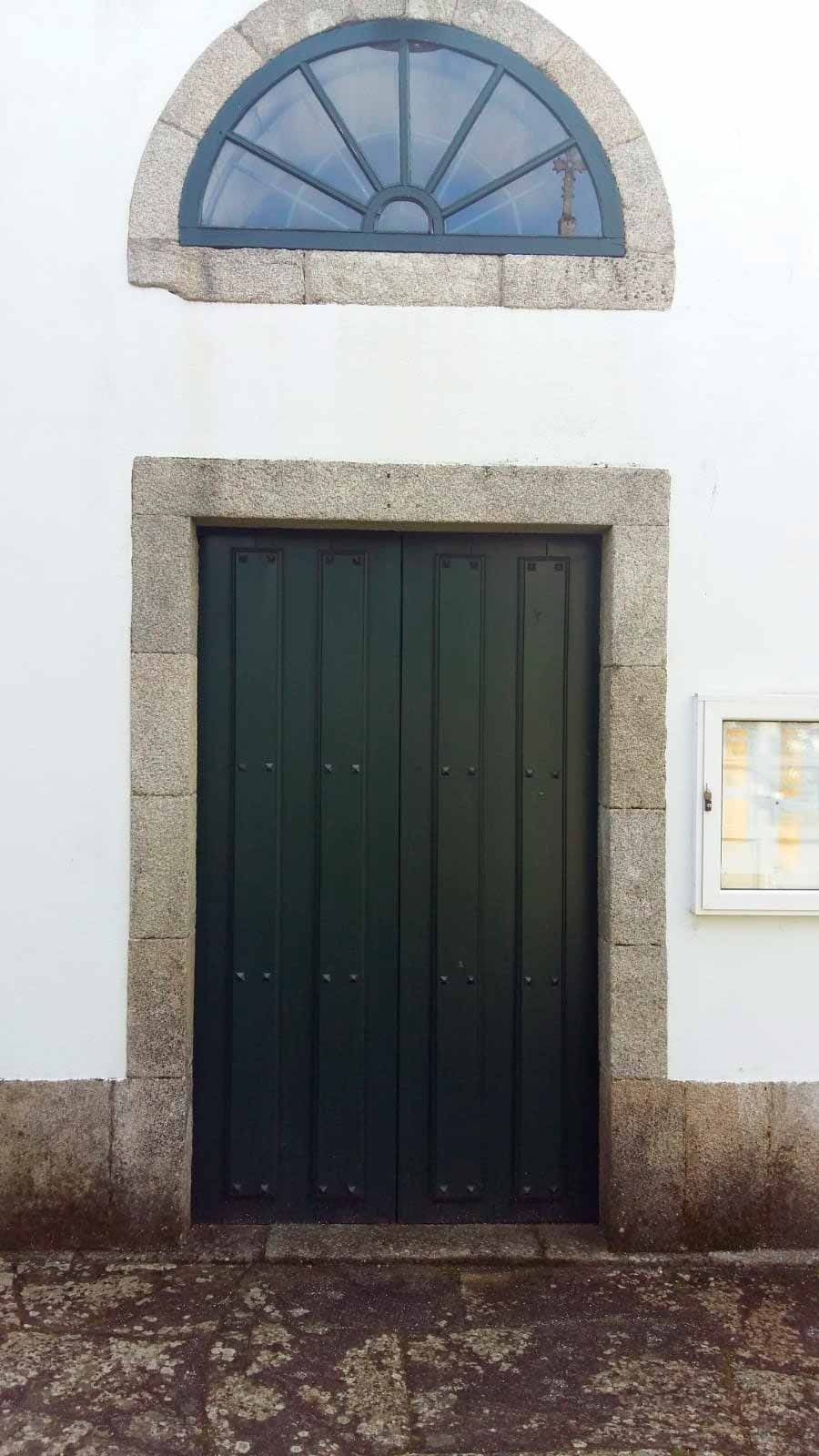 Una puerta verde con un arco de piedra y una ventana en un edificio blanco.