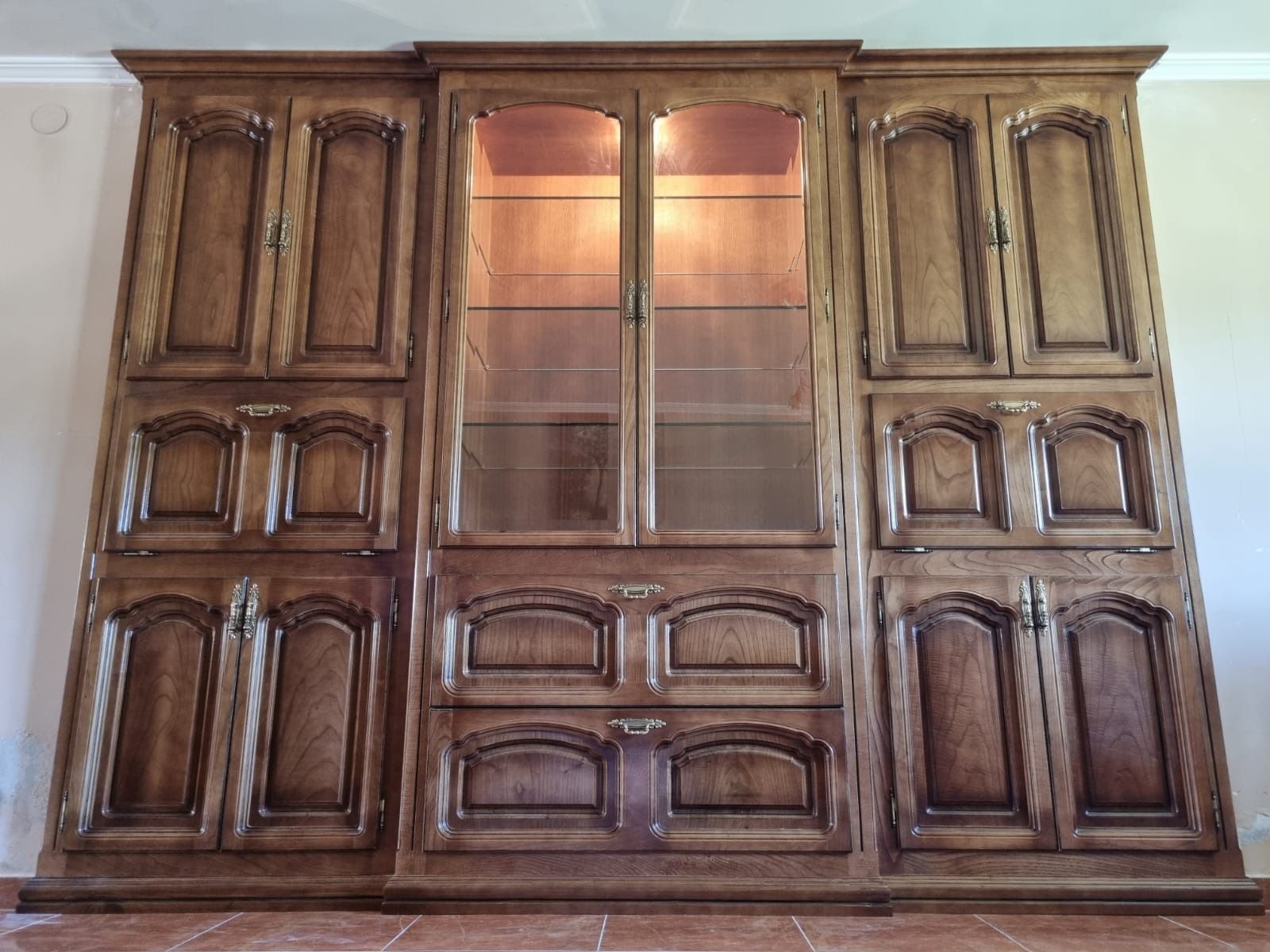Un gran armario de madera con puertas de cristal y cajones en una sala de estar.