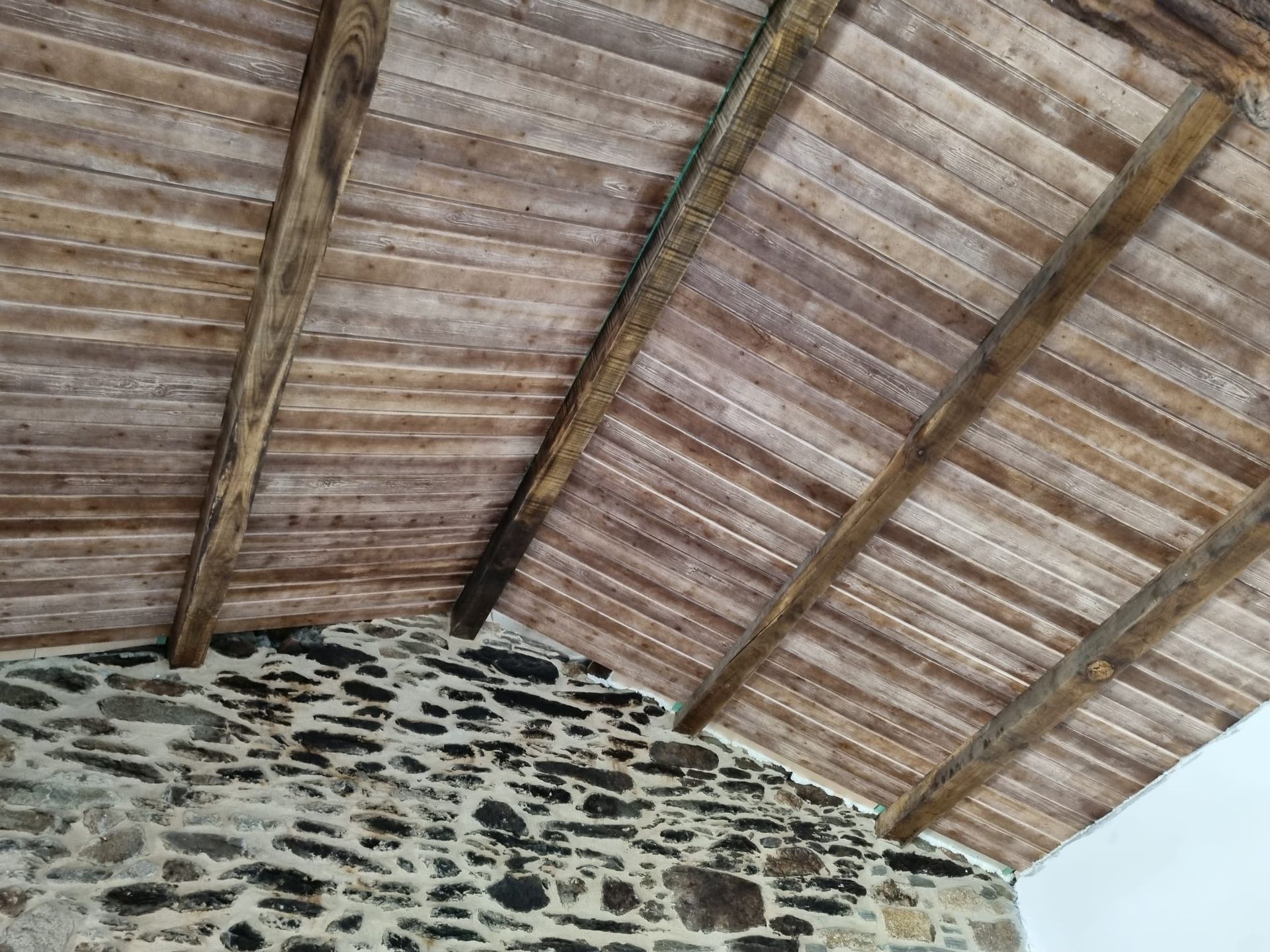Un techo de madera con una pared de piedra al fondo.