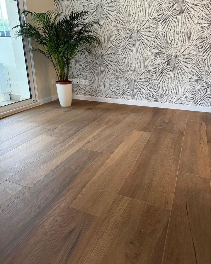 Pièce vide avec parquet, papier peint à motifs et une plante en pot près de la fenêtre