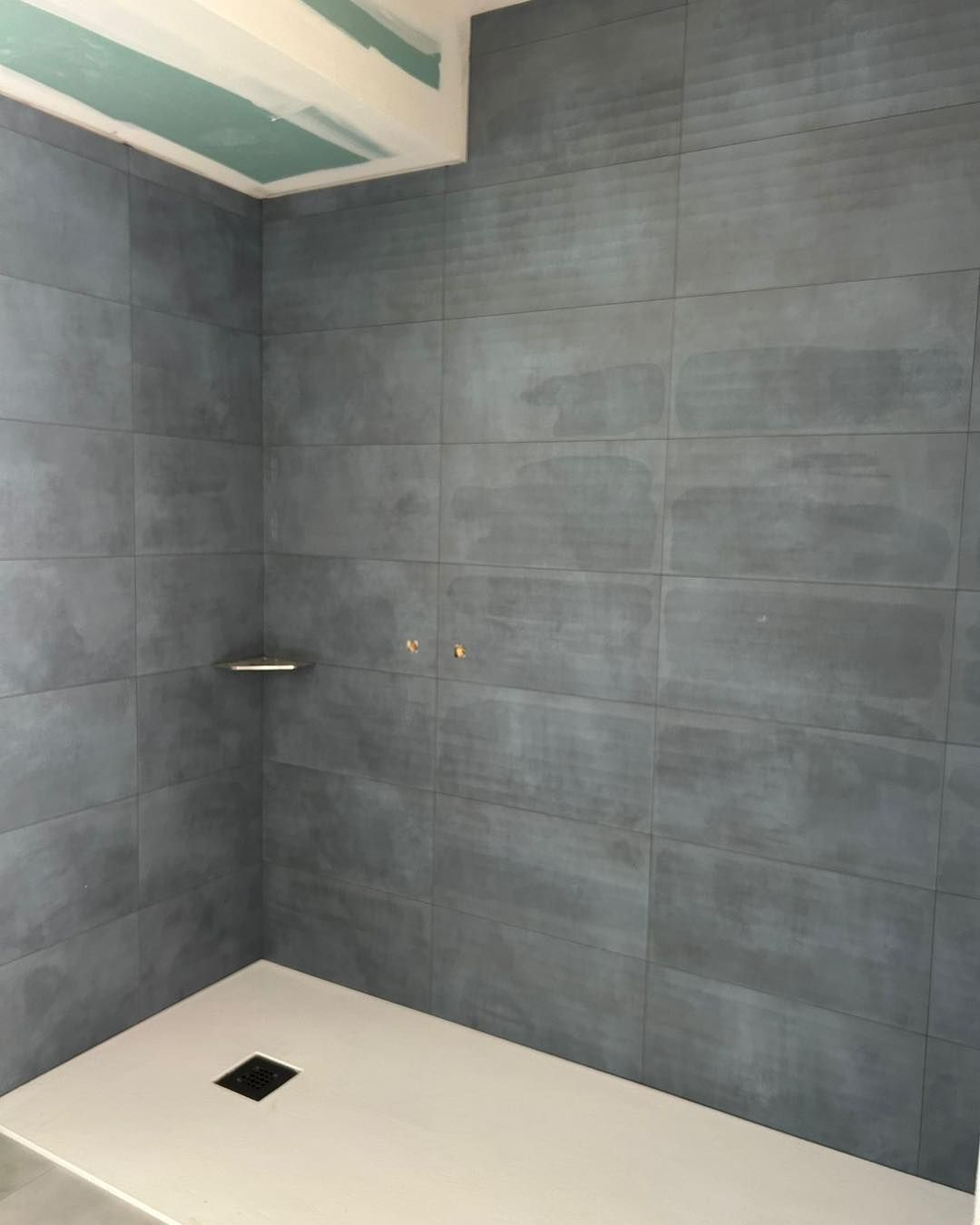 Douche carrelée grise en construction, avec receveur et bonde blancs.