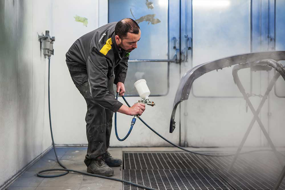 mécanicien en train de peindre une carrosserie au pistolet