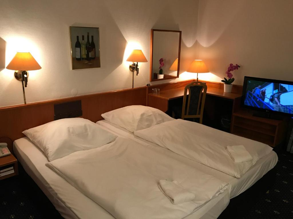 Ein Hotelzimmer mit zwei Betten, einem Schreibtisch und einem Fernseher. Beleuchtet von warmen Lampen.