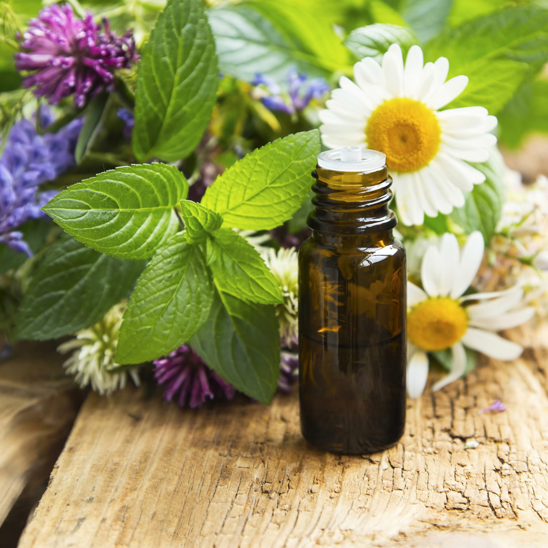Flacone di olio essenziale in ambra con erbe e fiori su una superficie di legno.