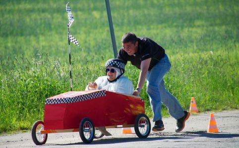 Eine ältere Person in einem roten Güterwagen wird während eines Rennens von einem Mann geschoben.