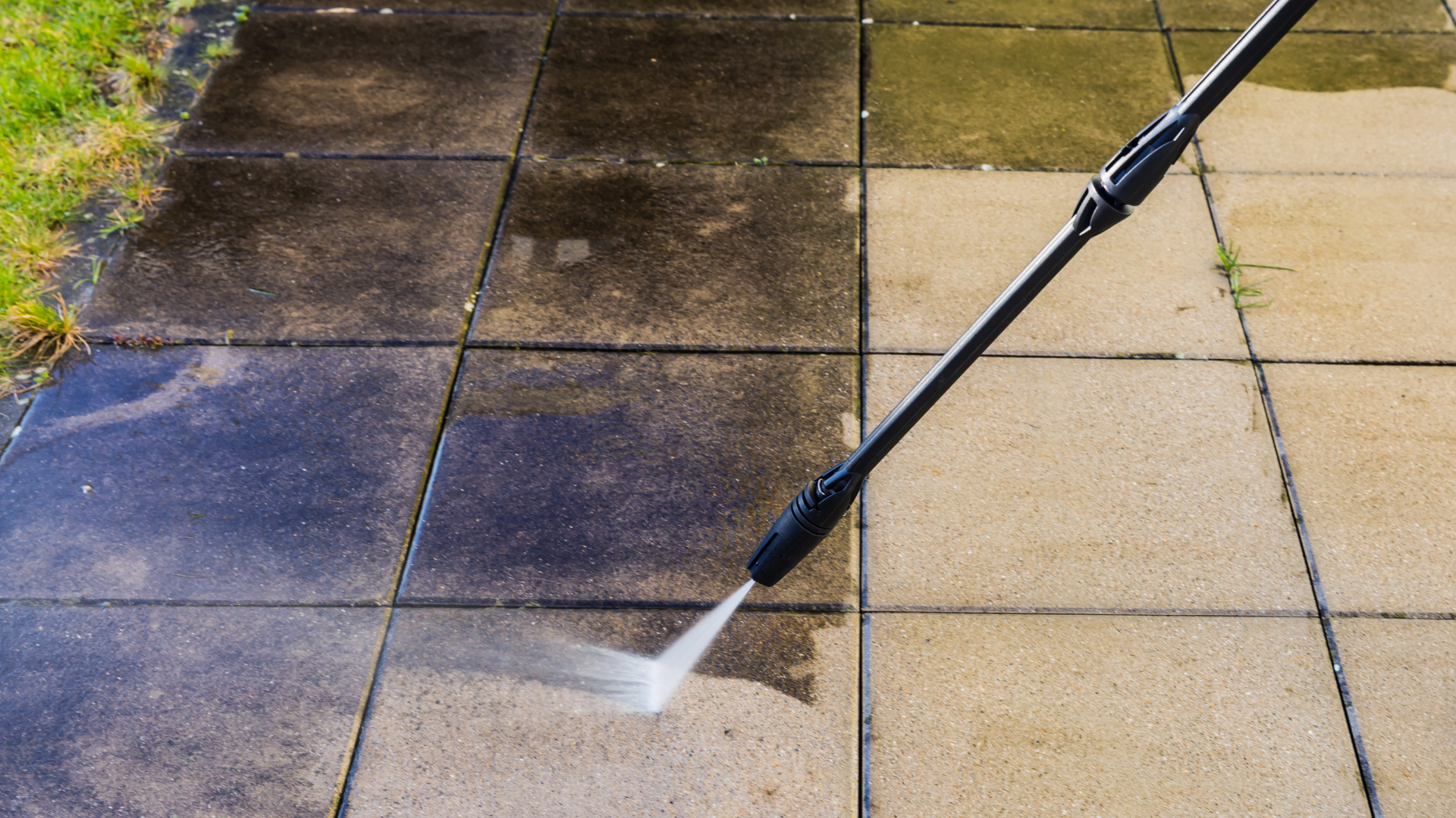 Une personne nettoie à haute pression un toit en tuiles rouges à côté d'une cheminée en briques et d'un puits de lumière.