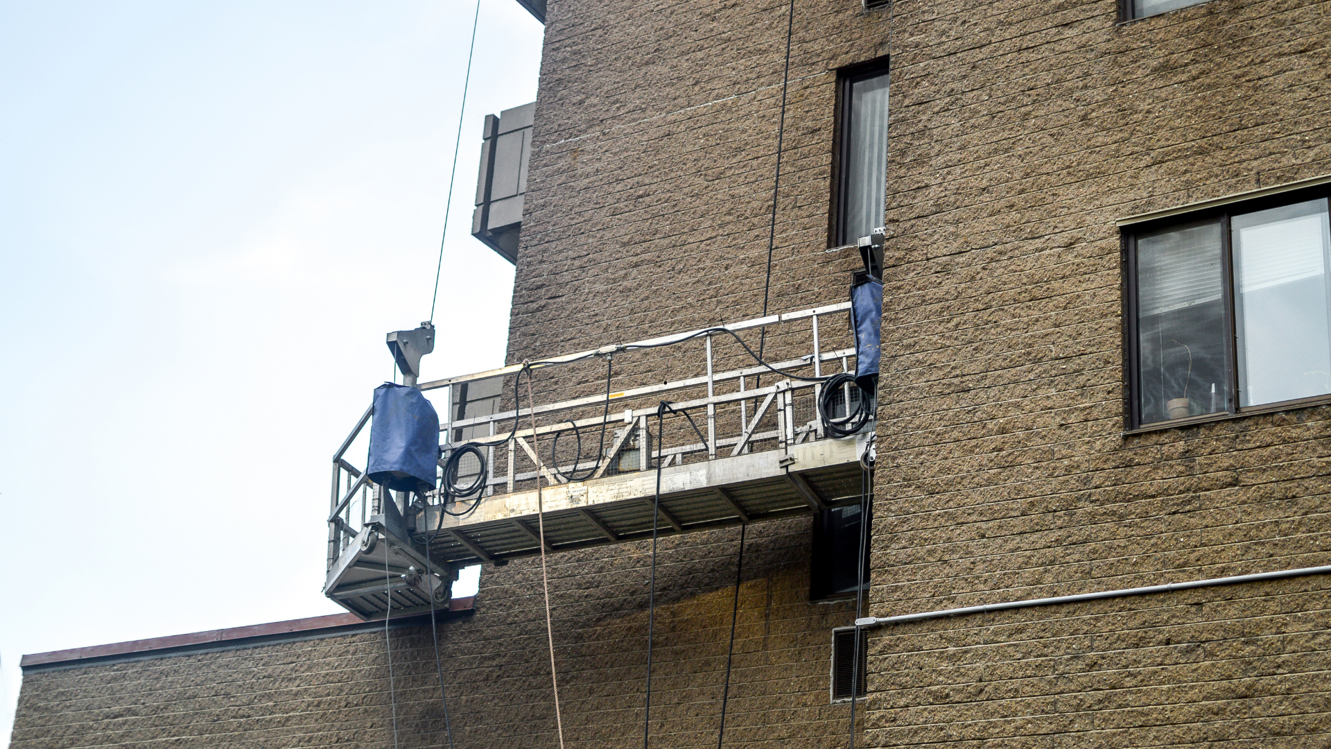 Des ouvriers sur un échafaudage suspendu nettoient ou réparent l'extérieur en briques d'un bâtiment.