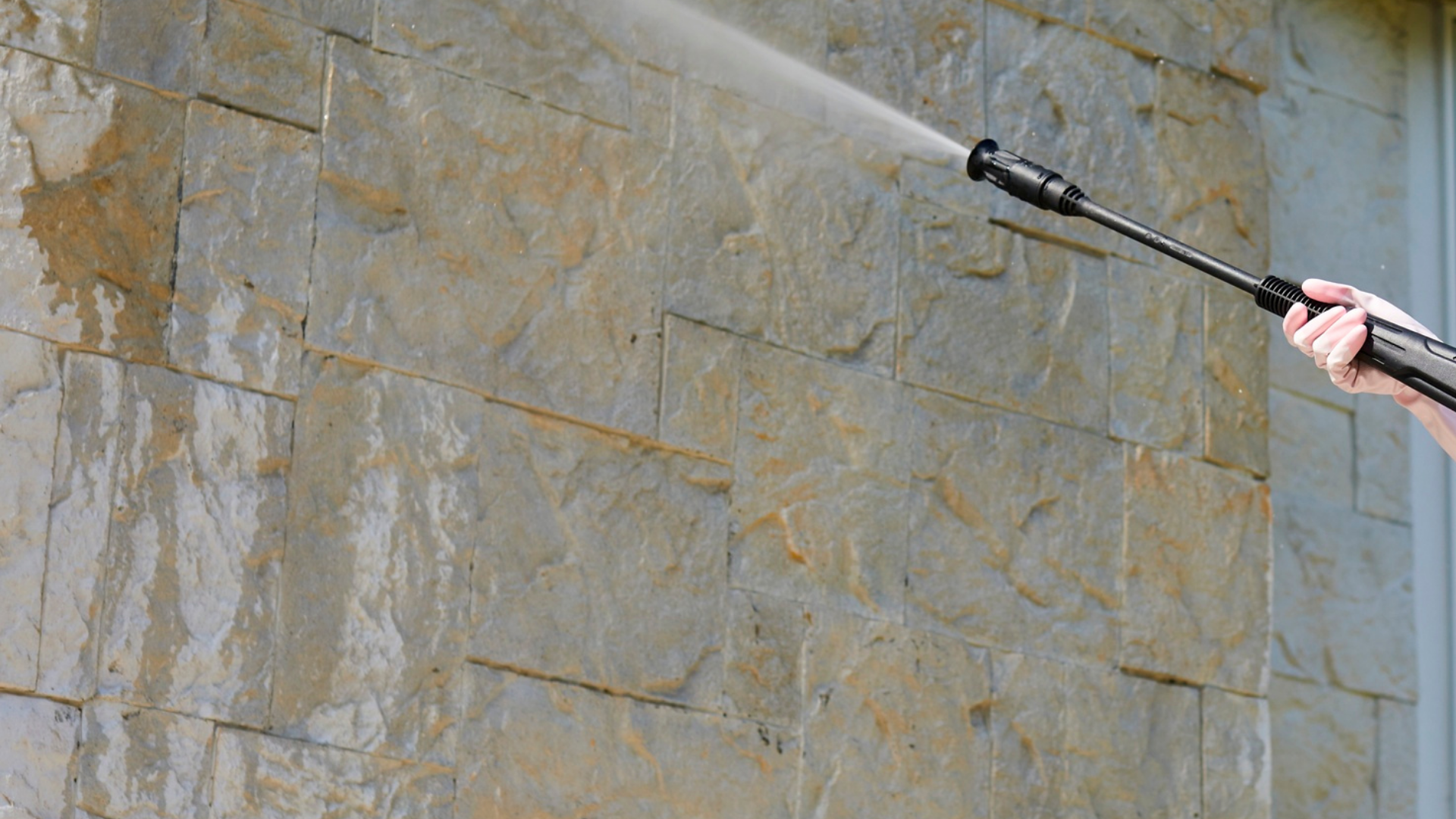 Personne utilisant un nettoyeur haute pression pour nettoyer un mur en pierre beige.