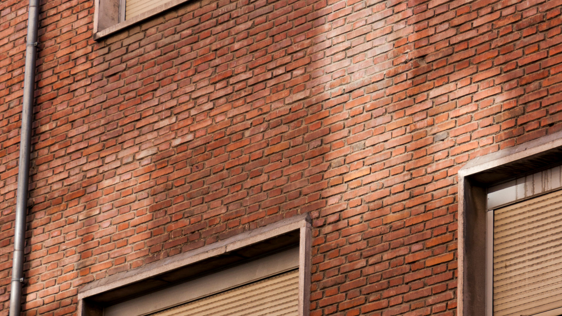 Bâtiment en briques rouges avec deux stores fermés ; ombres sur la brique.