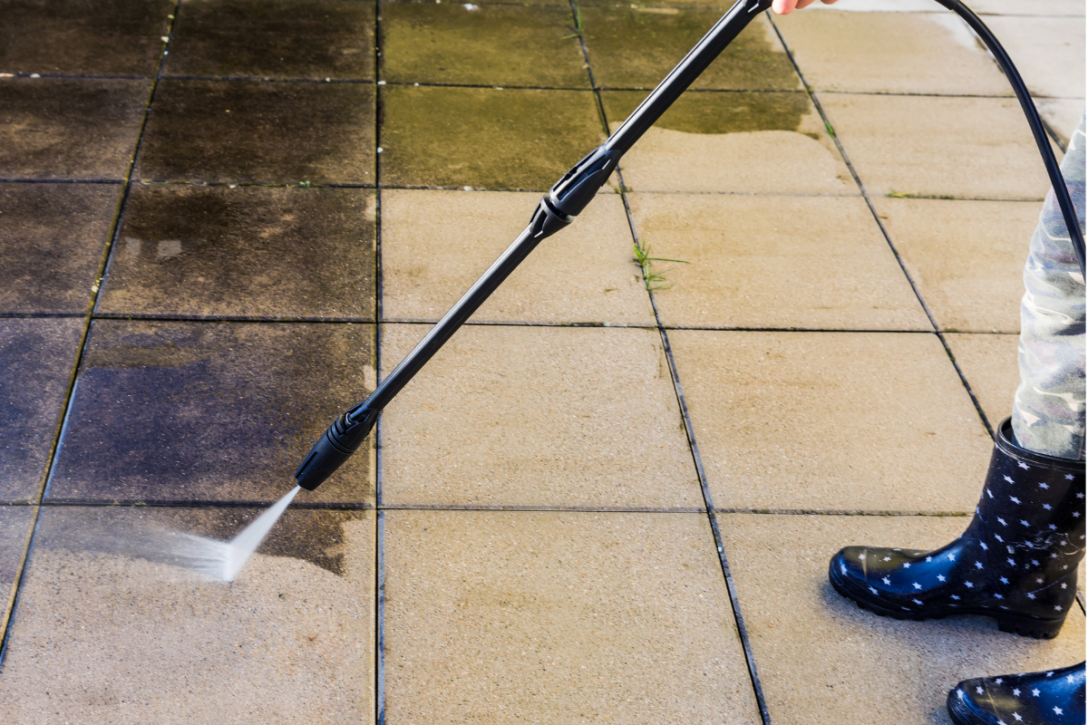 Une personne nettoie à haute pression une terrasse sale, en nettoyant les carreaux avec un jet haute pression.