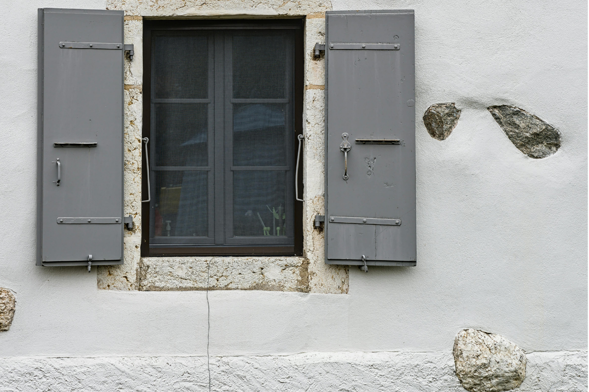 Fenêtre aux volets gris sur un bâtiment en pierre blanche.