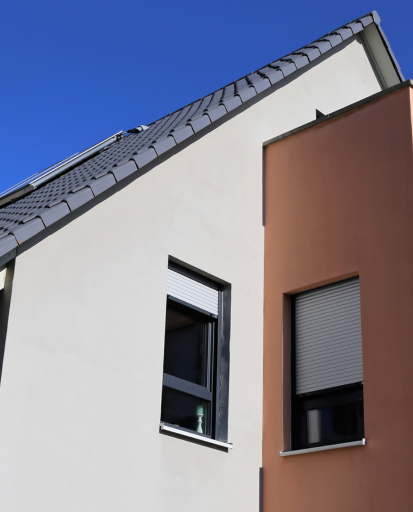 Extérieur d'un bâtiment moderne, murs blancs et marron, deux fenêtres, toit gris foncé contre un ciel bleu.