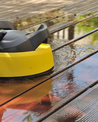 Nettoyeur haute pression jaune et noir nettoyant une terrasse en bois humide.