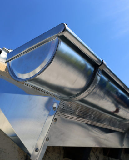 Bordure de gouttière et de descente pluviale métallique et brillante contre un ciel bleu clair.