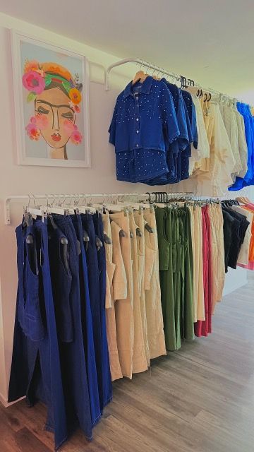 Kleiderständer mit Outfits in verschiedenen Farben; an der Wand hängt ein gerahmtes Porträt von Frida Kahlo.
