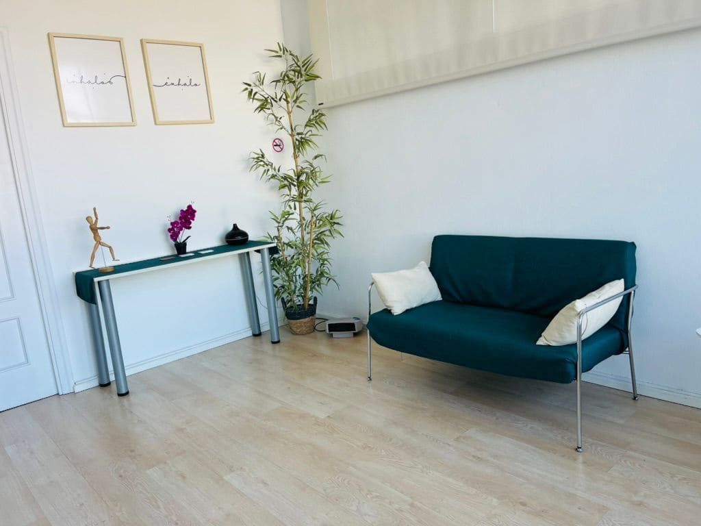 Una habitación minimalista con un sofá color turquesa, una mesa consola con objetos decorativos, una planta en maceta y dos láminas enmarcadas en la pared.