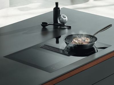 Moderne Kücheninsel mit integriertem Kochfeld und Dunstabzug, Essen brutzelt in der Pfanne.