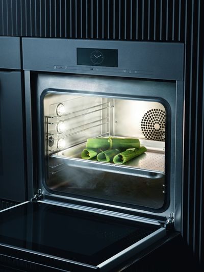 Der Backofen ist geöffnet, Lauch liegt auf einem Backblech, der Dampf ist sichtbar. Der Innenraum ist mit Rosten und einem Ventilator beleuchtet.