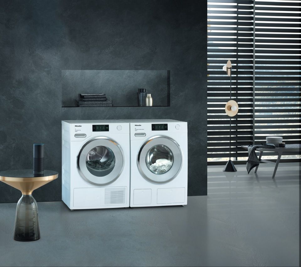 Weisse Waschmaschine und Trockner in einem modernen Waschraum mit dunkelgrauen Wänden und Tageslicht.