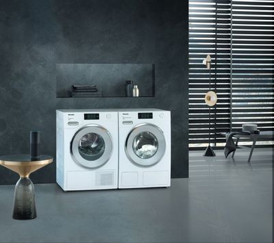 Weisse Waschmaschine und Trockner in einem modernen Waschraum mit dunkelgrauen Wänden und Tageslicht.