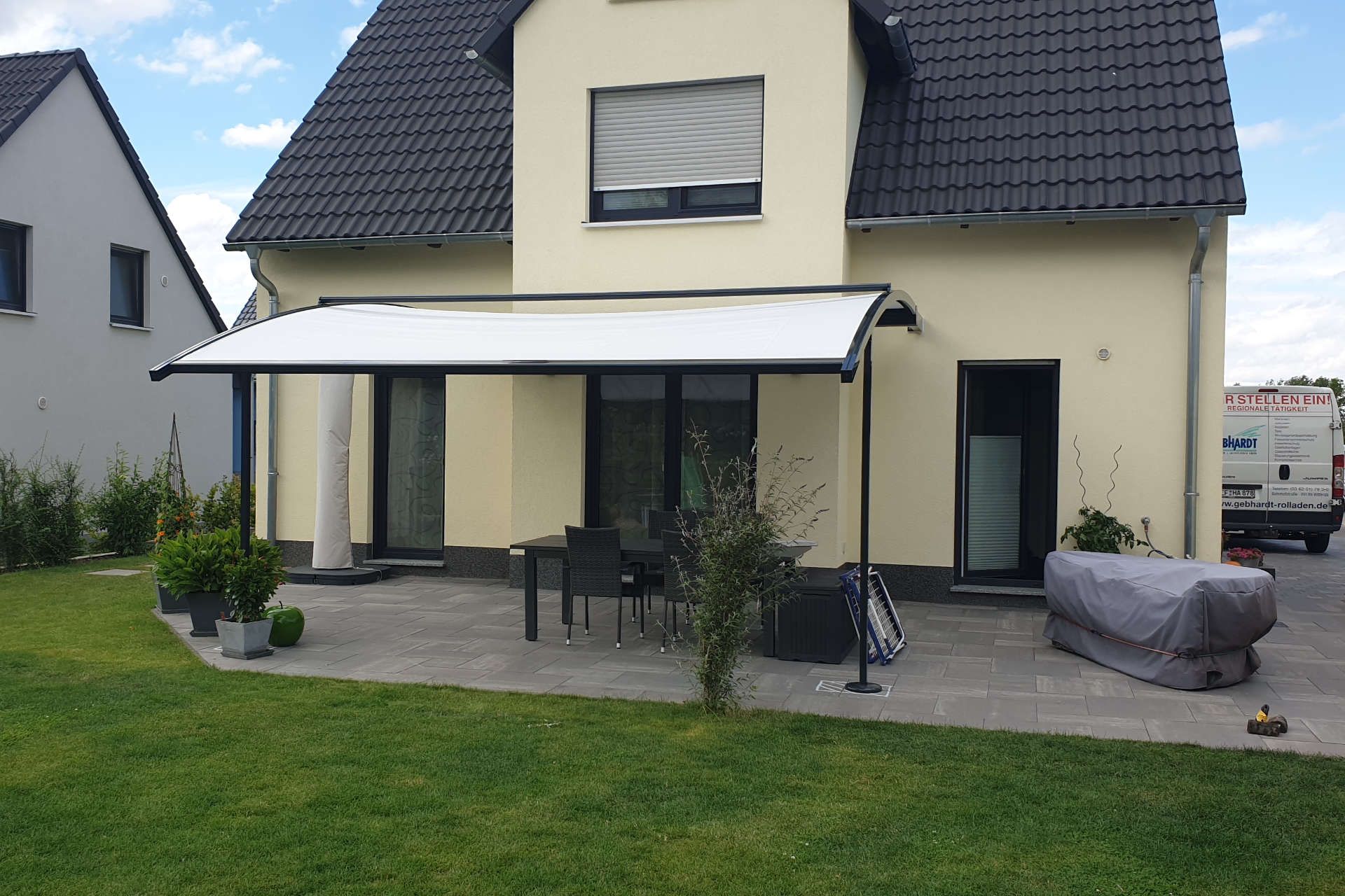 Ein weißes Haus mit schwarzem Dach und weißer Markise.