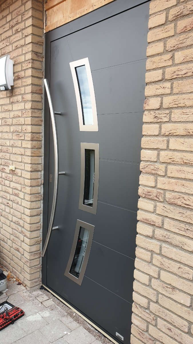An einer Ziegelwand hängt eine schwarze Tür mit einem Edelstahlgriff.