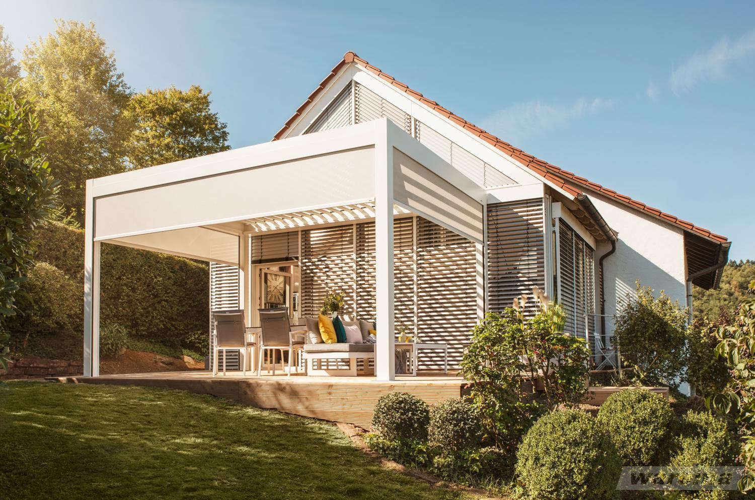 Ein weißes Haus mit einer Pergola im Hinterhof.