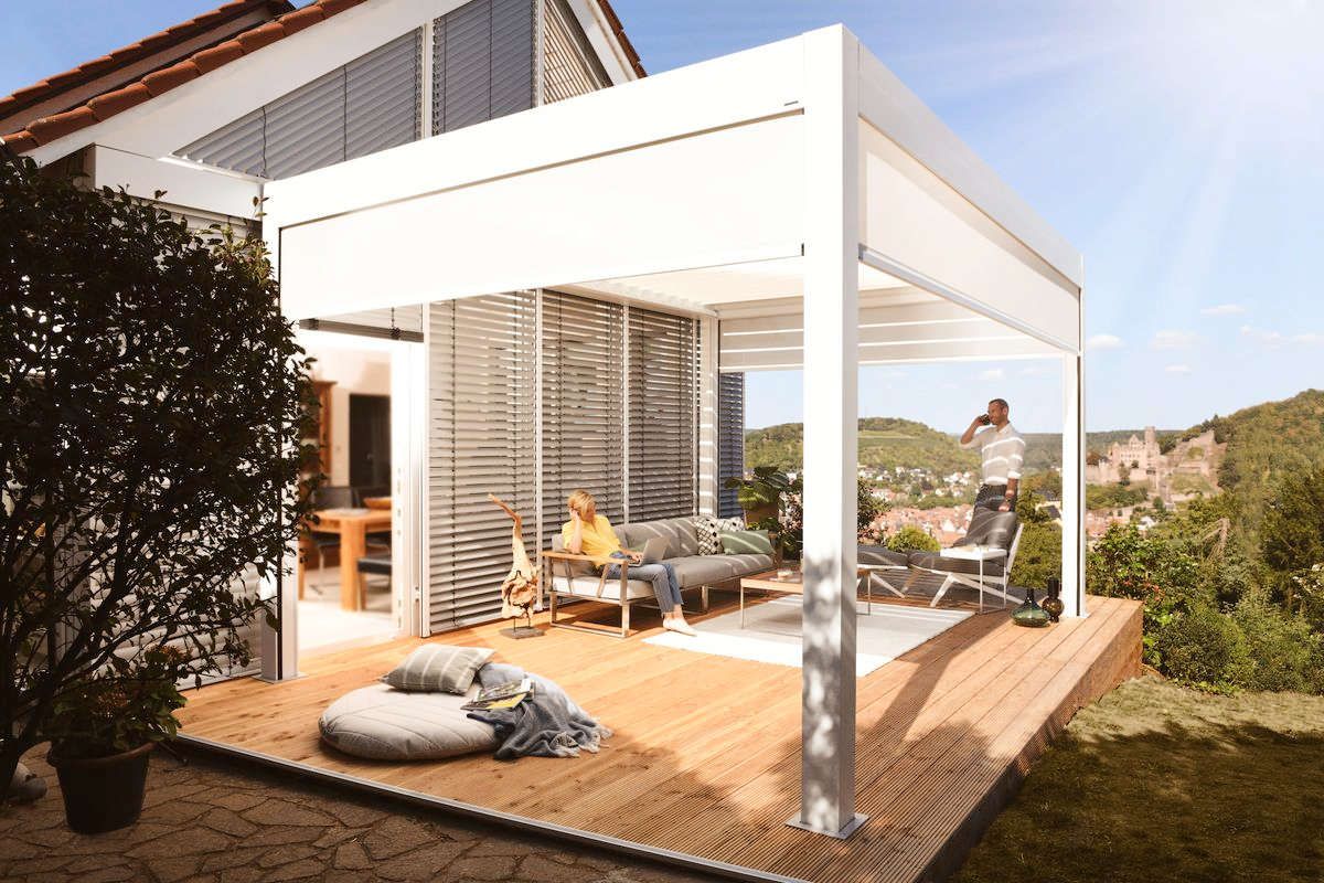 Eine Frau sitzt auf einem Sofa auf einer Terrasse unter einer Pergola.